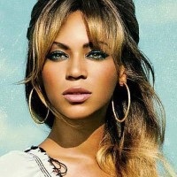 photo de Beyoncé (tête et épaules) les cheveux attachés en queue de cheval, une frange longue sur les côtés, bien maquillée (mascara, eyeliner, fard à paupières bleu-vert, fond de teint orange, fard à lèvres rose, peau parfaitement lisse), portant des créoles et on devine une robe ou un chemisier en mousseline blanc à coutures noires